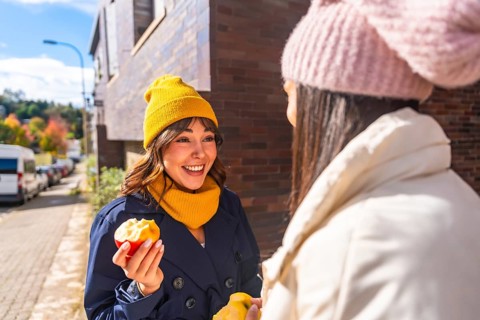 Two cheerful women friends enjoying fresh apples and engaging in a conversation outdoors on an