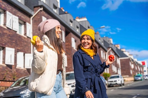 Two smiling young women friends wearing warm autumn clothing and beanies, walking outdoors in the