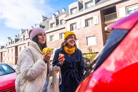 Two young adult women friends enjoying a healthy snack of apples while walking on a city street,