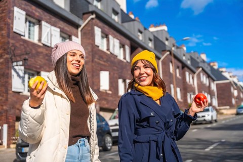Two smiling young women friends are enjoying a sunny winter day, walking along a city street and