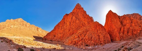Panoramic view of bright red rocks in desert landscape under clear sky, Todra Gorge in Morocco