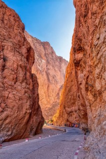 Narrow road leads through dramatic red rock formations at dusk, Todra Gorge in Morocco
