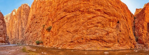 Panoramic view of gigantic red rock face under clear sky, Todra Gorge in Morocco
