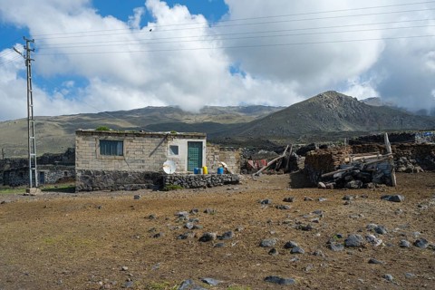 A simple stone house with power lines in a mountainous landscape, village at the foot of Great