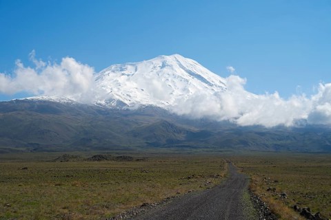 A snow-covered mountain under blue sky with a path in the foreground, near Cevirme, Great Ararat,