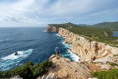 Tourist enjoying the view of steep cliffs by the sea, coastal landscape, cliffs on the Capo Caccia