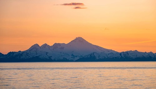 View of Cook Inlet on white mountain peaks of Mount Iliamna at sunset, picturesque golden light of