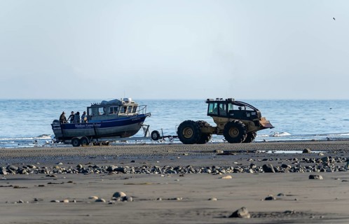 Motor boat on a boat trailer is driven into water by a tractor on a beach, Anchor Point, Alaska,