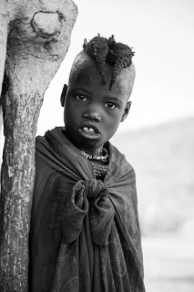 Black and white, Himba girl leaning at a traditional clay hut, in the morning, traditional Himba