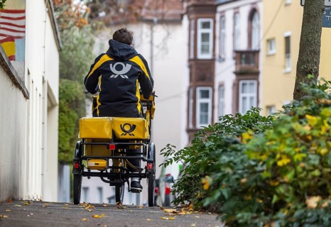 Deutsche Post mailmen on a bicycle through the city. Stuttgart, Baden-Württemberg, Germany