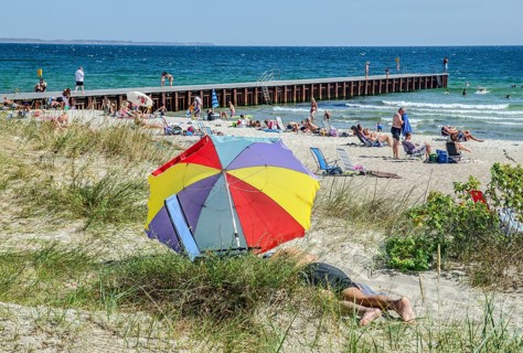 Colorful parasol on the beach with jetty and sunbathing people in Ystad, Skåne County, Sweden,