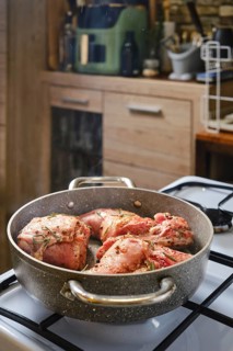 A rabbit's hind leg and saddle is simmering in a skillet, seasoned with herbs, on a gas stove in a