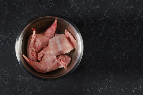 Fresh rabbit hind legs and a saddle are soaked in water with vinegar in a metal bowl. The process