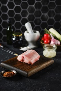 A raw rabbit saddle loin on a wooden cutting board in a kitchen setting. Fresh vegetables and