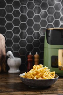 Freshly cooked golden fries are piled in a rustic bowl placed on a wooden kitchen counter. A