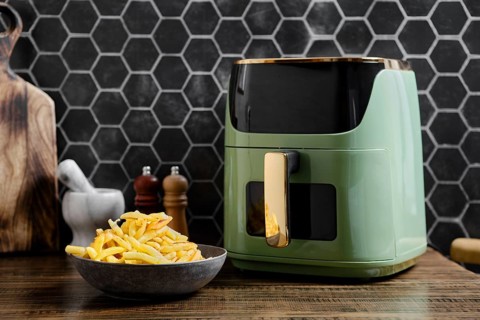 A sleek air fryer is on a wooden countertop in a contemporary kitchen. A bowl of golden, crispy