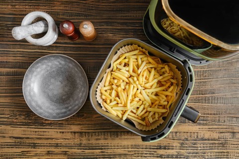 Golden fries are freshly cooked in an air fryer, resting in a basket lined with paper. A ceramic