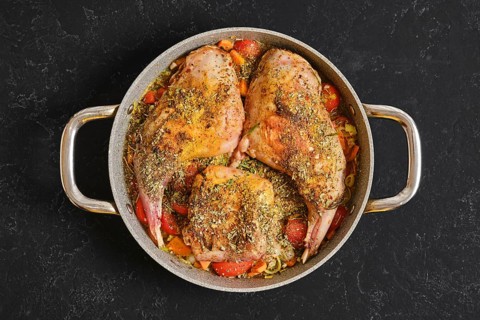 Two rabbit hind legs and a saddle are seasoned with herbs and spices, placed on a bed of colorful