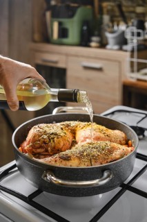 Close-up view of hand pouring dry white wine in a pot with rabbit hind legs and saddle