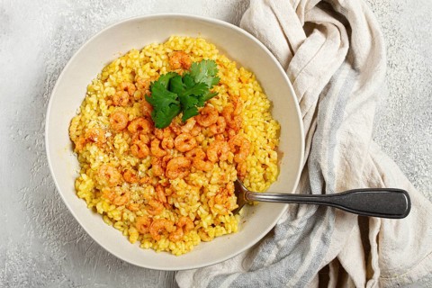 Risotto with shrimp, in a bowl, on a textured surface, with a side dish of fresh coriander,