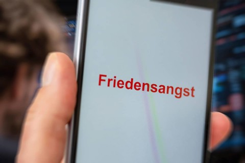 (photo montage) Smartphone with displayed text FEAR OF PEACE against the backdrop of a stock