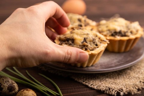 Tartlets with meat and cheese with hand on brown wooden background and linen textile. side view,