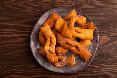 Crunchy biscuit Brushwood cookies sprinkled with powdered sugar on brown wooden background, top