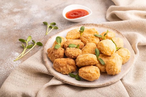 Fried crispy Chicken Nuggets with ketchup, microgreen on brown concrete background and linen