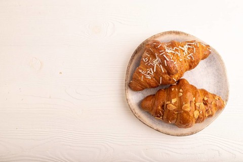 Croissant on blue plate on white wooden background, top view, flat lay, copy space