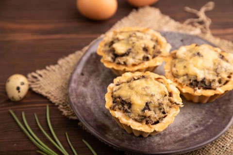 Tartlets with meat and cheese on brown wooden background and linen textile. side view, close up,