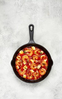 Greek saganaki, in an iron pan, saganaki with shrimp, shrimp in tomato sauce, with pepper and feta