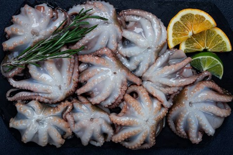 Fresh baby octopus, on black slate, with lemon and greenery, top view, no people