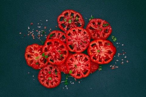 Freshly sliced ripe tomatoes arranged on a textured dark surface with herbs and salt scattered