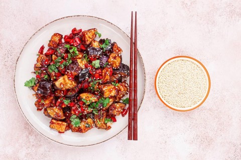 Fried eggplant, Chinese style, in sweet and sour sauce, with pepper and sesame seeds. on a white