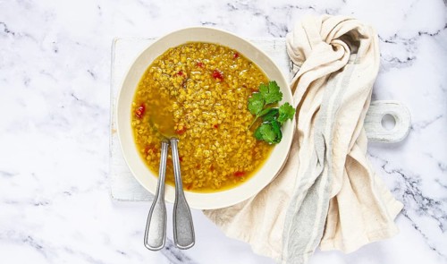 A bowl filled with hearty lentil soup sits on a marble surface, garnished with fresh herbs. A cloth