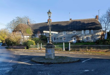 Historic signpost with direction arrows, thatched cottages in village of Pewsey, Wiltshire,