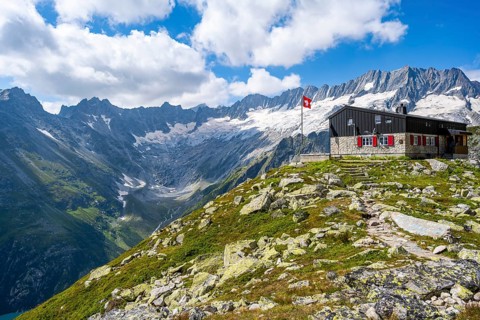 Mountain hut Bergseehütte with Swiss flag in picturesque mountain landscape, view of Damma Glacier