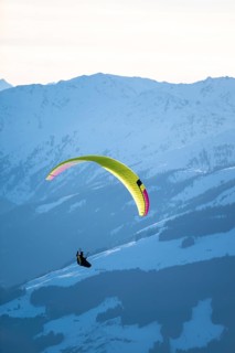 Paragliders flying over snowy mountain peaks in winter in evening light, Kitzbühel Alps, Tyrol,