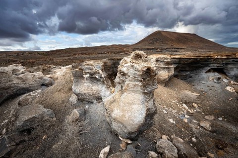 Eroded rock formations in volcanic landscape with dramatic cloudy skies, Ciudad Estratificada or