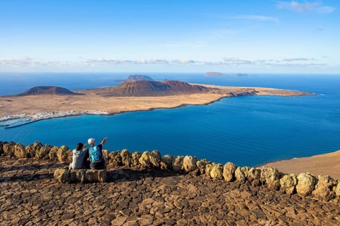 Tourists on a bench on the viewing platform at the Mirador del Río viewpoint, in the evening light,