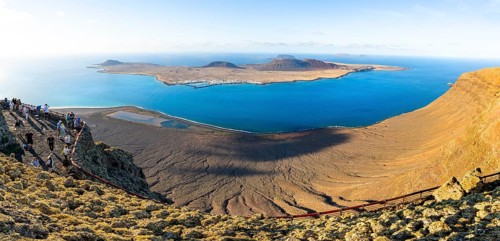 View of La Graciosa island with volcanic craters in the evening light, tourists on an observation