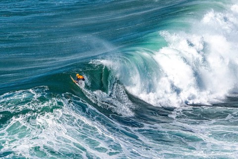 Surfers with their jet ski pilots in the Atlantic waves below Farol de Nazaré, Forte São Miguel,