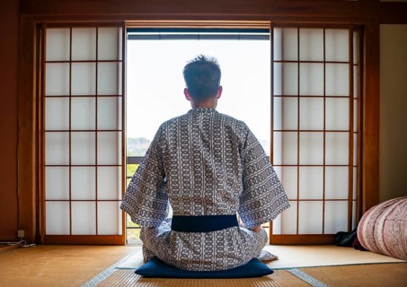 Young man wearing kimono sitting in traditional Japanese living room with tatami mats and shoji