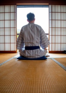 Young man wearing kimono sitting in traditional Japanese living room with tatami mats and shoji