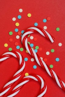 Candy canes and sugar confetti against red background, Christmas