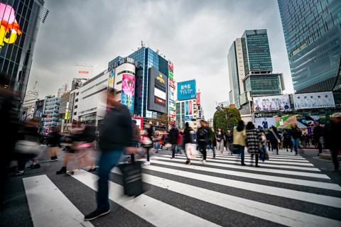 Crowd crossing zebra crossing on a large intersection, motion blur, back modern houses with