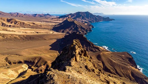 Desert landscape converges with ocean along a rugged coastal area, shore break at cliffs, blue