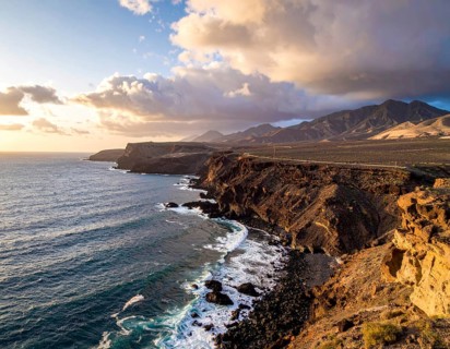 Desert landscape converges with ocean along a rugged coastal area, shore break at cliffs, blue