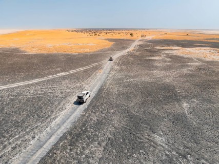 Aerial view, two off-road cars driving on a salt pan, arid landscape, Botswana