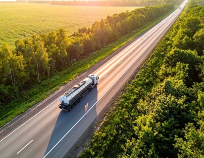 Petrol cargo truck lorry tanker driving on highway hauling oil products at sunrise, wide hilly